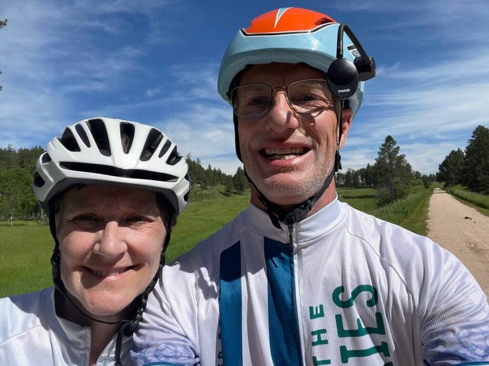 Two cyclists smiling on a country road by their camper