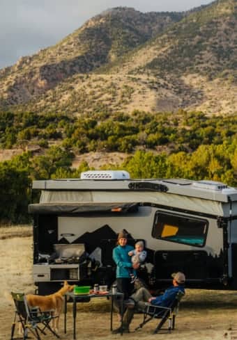 Family relaxing beside their camper in the mountains