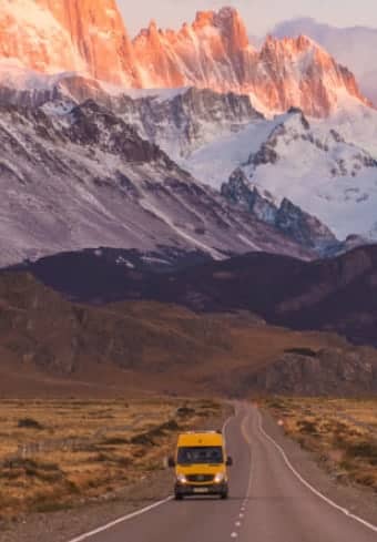 Yellow camper van on an open road below the snow-capped Fitz Roy massif in Patagonia